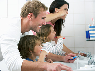 Eine junge Familie gemeinsam im Badezimmer beim Zähneputzen.